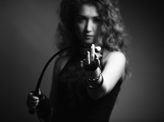 Beautiful sexy domineering woman holding a whip in her hands She is dressed in a corset and and gloves. BDSM. In sharpness, the hand and the tip of the whip. - obrazy, fototapety, plakaty