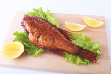 Smoked fish and lemon on green lettuce leaves on Wooden cutting board isolated on white background.