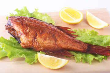 Smoked fish and lemon on green lettuce leaves on Wooden cutting board isolated on white background.