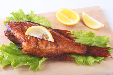 Smoked fish and lemon on green lettuce leaves on Wooden cutting board isolated on white background.