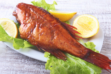 Smoked fish and lemon on green lettuce leaves on Wooden cutting board isolated on white background.