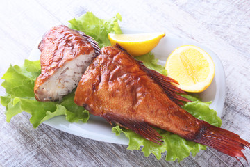 Smoked fish and lemon on green lettuce leaves on Wooden cutting board isolated on white background.