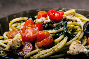 Spaghetti pasta with olive oil, tomatoes, herbs, chilly, and cut chicken breast. Italian cuisine. Plate with food on a black table. 