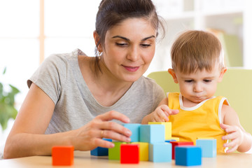 Young mummy and her kid play with cubes toys in nursery
