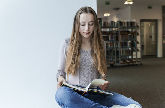 Teenage girl reading book in a public library