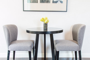 Yellow flowers in the vases on the table and chairs by the wall.
