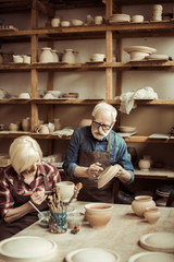 Woman painting clay pot with senior potter at workshop