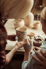 Close up of girl painting clay pot and grandparents helping at workshop