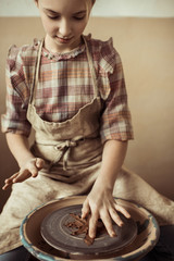 Front view of little girl making pottery on wheel at workshop