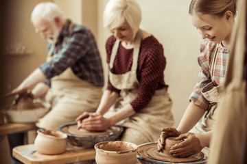 Grandmother and grandfather with granddaughter making pottery at workshop