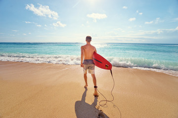 It's time for surfing! Young man holding surf board on the sea shore.