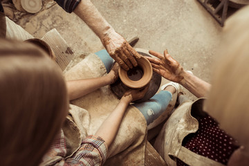 Overhead view of little girl making pottery on wheel with help of grandparents at workshop