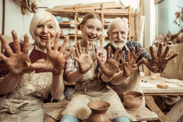 Grandmother and grandfather with granddaughter showing hands in clay in workshop