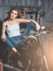 Plakat girl biker sitting on vintage motorcycle in garage