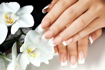 Female hands with white nails on background of white flowers. - obrazy, fototapety, plakaty