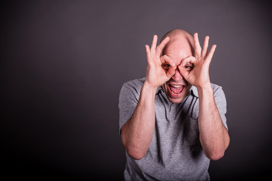 Mann mit grauem Poloshirt formt lachend mit seinen Fingern eine Brille, schreit dabei