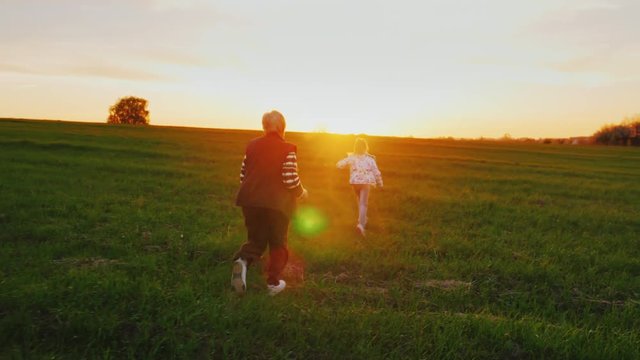 Active elderly people. Senior woman is running around with her granddaughter over a green meadow, playing dogganiks. On the Sunset. Concept - a healthy lifestyle, active old age