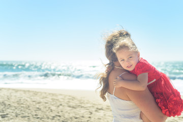 Mother hugging girl in red dress on the beach