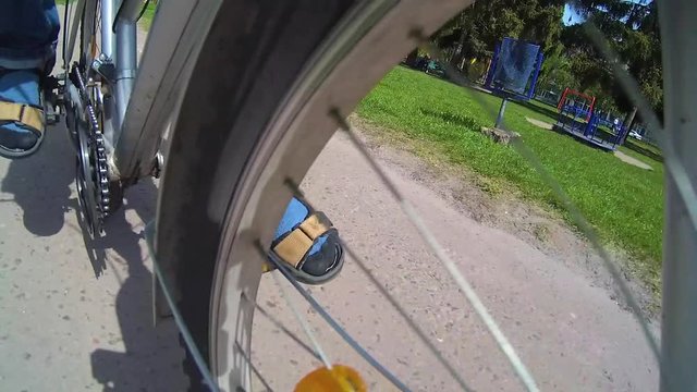 Closeup of wheels of bike. Caucasian kid of 10 year old riding bicycle outdoors in sunny spring urban park. Point of view wide angle video footage shot with action camera.