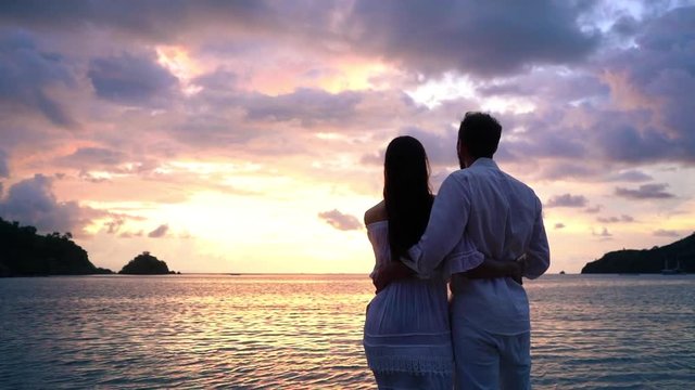 Paar in wei&szlig;er Kleidung betrachtet am Strand den Sonnenuntergang - slow motion