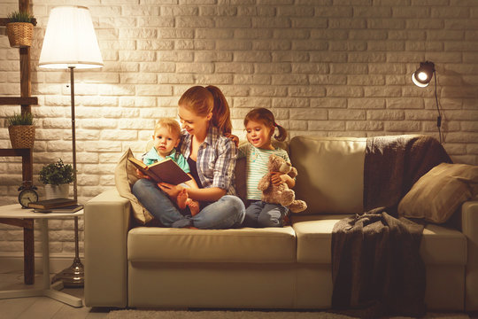 Family before going to bed mother reads children book about lamp in evening