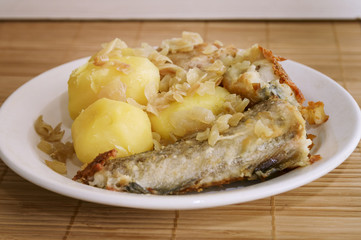 Fried fish and boiled potatoes lies on a plate on a bamboo napkin. Close-up, selective focus.