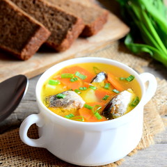 Light fish soup recipe. Delicious fish soup with potatoes, carrots and green onions in a bowl. Rye bread pieces, spoon on rustic wooden table. Closeup