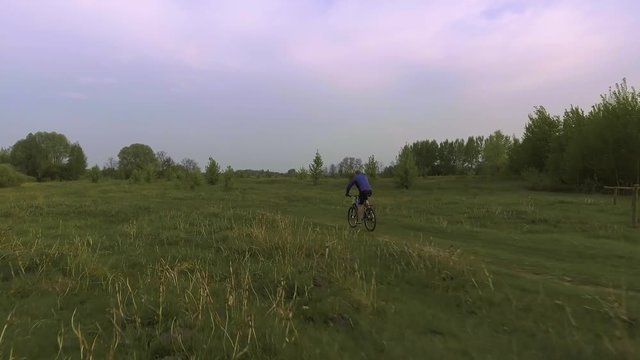 man cyclist rides on the spring green meadow
