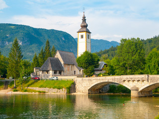 Church of St John the Baptist and old stone bridge at Lake Bohinj in alpine village Ribicev Laz, Julian Alps, Slovenia.