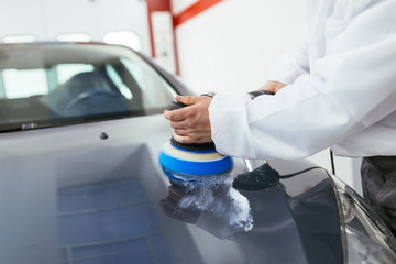 Car detailing - Hands with orbital polisher in auto repair shop. Selective focus. 