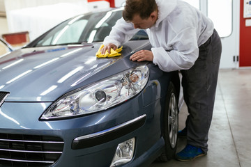 Fototapeta premium A man cleaning car with microfiber cloth, car detailing (or valeting) concept. Front lights protected with isolation blue tape. Selective focus. 
