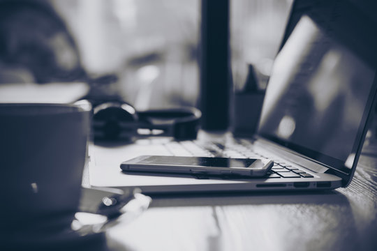 Black and white image of laptop , smart phone , coffee and headphone on wooden table in office