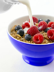 Pouring milk over muesli and fresh fruit, white background