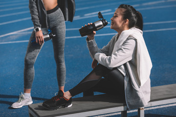 Fototapeta na wymiar Athletic young women in sportswear drinking water from sports bottles on stadium, running women concept