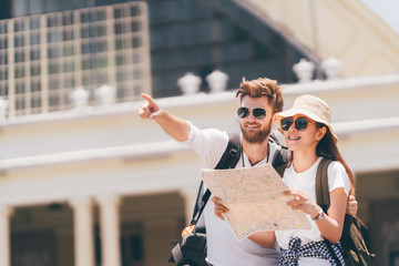 Multi-ethnic traveler couple using local map together on sunny day, man pointing forward to copy...