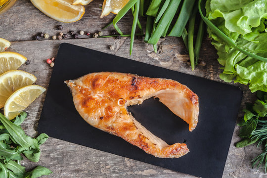 Baked steak trout fish on a stone board, around greens, leaves, 