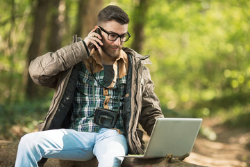 Busy young environmentalist is talking on the phone while working on laptop in the woods