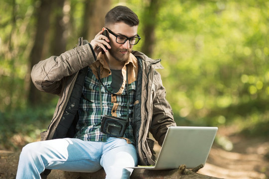 Busy Young Environmentalist Is Talking On The Phone While Working On Laptop In The Woods