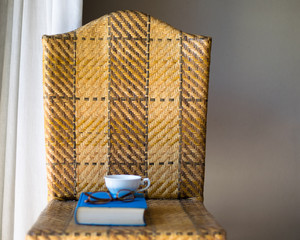 Book, cup and eyeglasses on a chair.