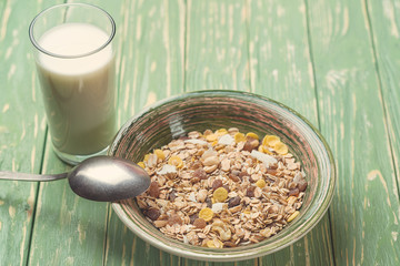 Bowl of oat flakes and glass of milk, on wooden background. Toned.