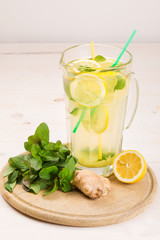 A glass decanter with a summer refreshing lemonade made of lemons and ginger with mint added on a...