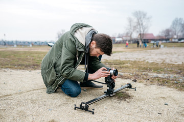 Obraz premium The cameraman shoots on the camera, outdoors. Sits on his knees and look into the lens