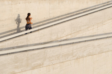 Sporty fitness young woman running up an urban ramp. Female fit runner training outside.