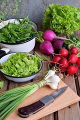 Fresh spring vegetables: radish, green and purple lettuce, onions, arugula on a wooden background. Preparation of food, salad. Healthy food.