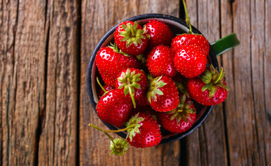 Fresh Strawberries in a Green enamel Cup on Vintage Wooden Background..Food or Healthy diet concept.Vegetarian.Copy space for Text. selective focus