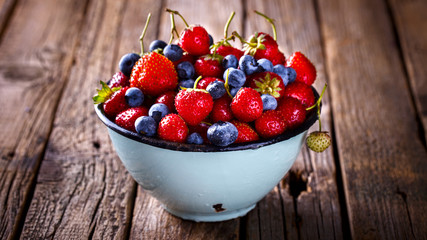 Fresh Strawberries and Blueberries  in the Iron bowl  on Vintage Wooden Background.Business Desk.Food or Healthy diet concept.Copy space for Text. selective focus.