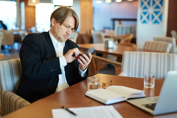 Portrait of confident middle-aged white collar worker dialing number of his business partner while working in cyber cafe