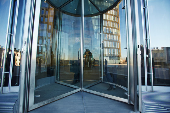 Full-length Portrait Of Senior Businessman Walking Through Revolving Door Of Office Building