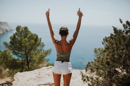 woman standing with hands up in front of the sea