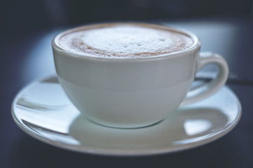 Closeup image of a white cup of hot coffee on vintage wooden table